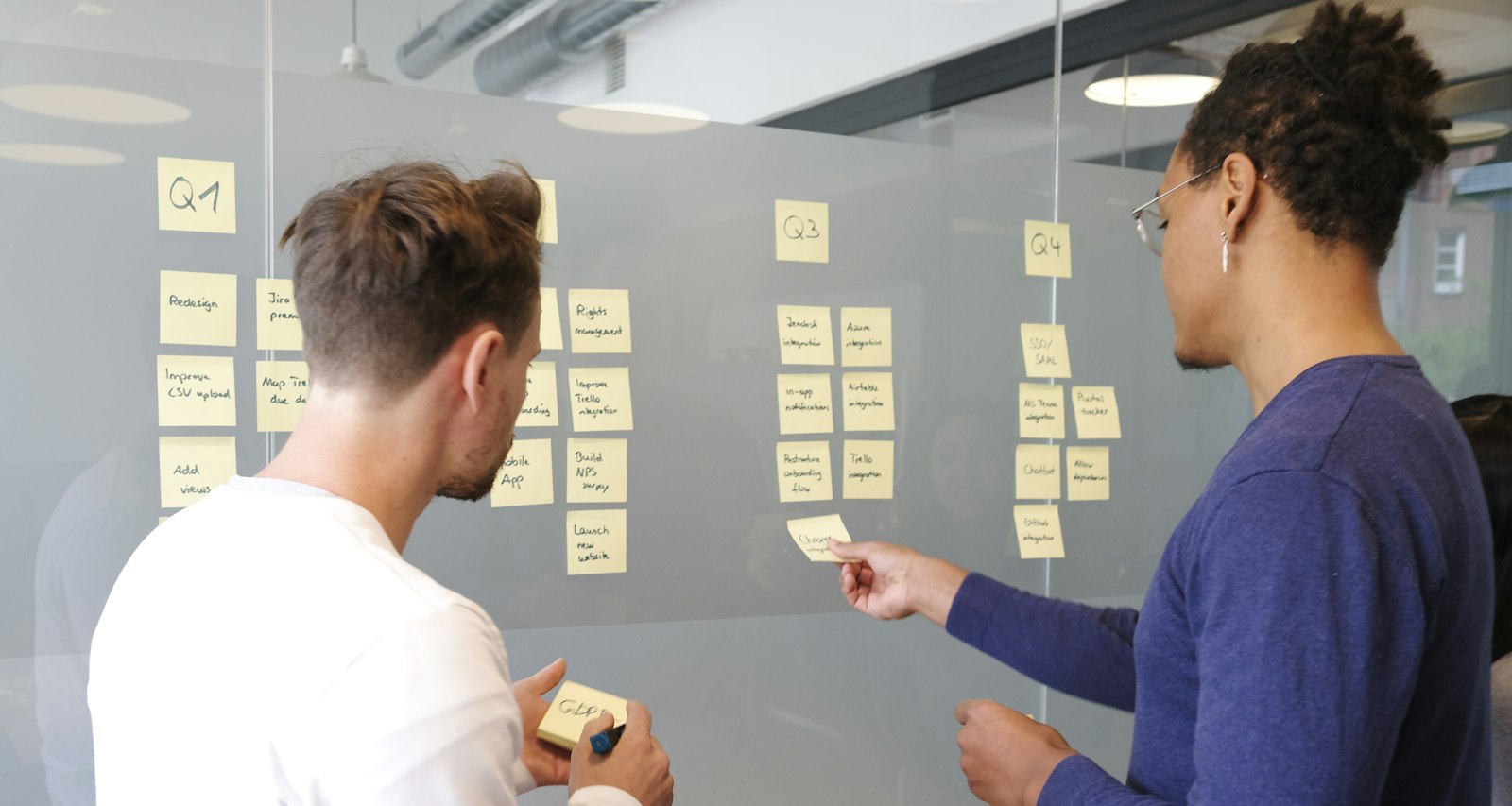 Two colleagues planning work with sticky notes on a glass wall